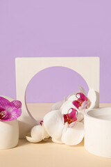 Decorative plaster podiums and beautiful orchid flowers on beige table against lilac background