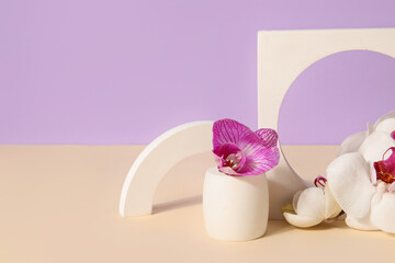 Decorative plaster podiums and beautiful orchid flowers on beige table against lilac background