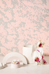 Decorative plaster podiums and beautiful orchid flowers on white table near pink wall