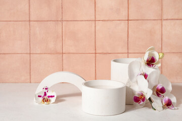 Decorative plaster podiums and beautiful orchid flowers on white table near tiled wall