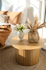 Vases with flowers and pampas grass on table in light bedroom