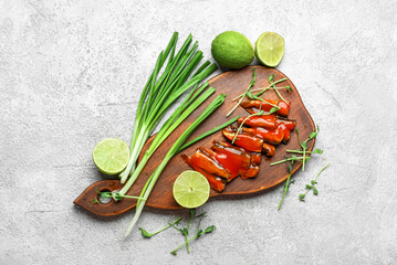 Board with canned fish in tomato sauce, lime, scallions and microgreens on grey table