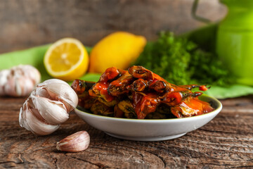Plate with canned fish in tomato sauce and garlic on wooden table