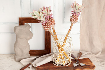 Vase with decorative pineapples, spatulas and decor on table near light wall