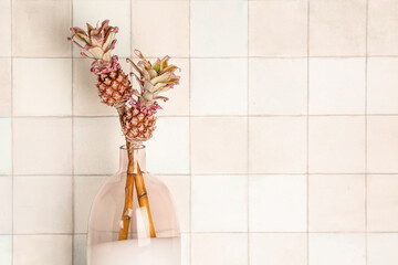 Vase with decorative pineapples near white tile wall