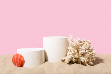 Decorative plaster podiums, seashell and coral in sand on pink background