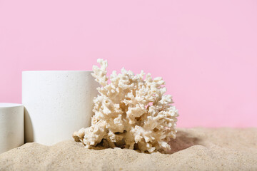 Decorative plaster podiums and coral in sand on pink background