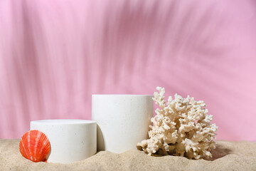 Decorative plaster podiums, seashell and coral in sand on pink background