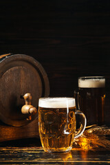 Mug of cold beer and wooden barrel on dark background
