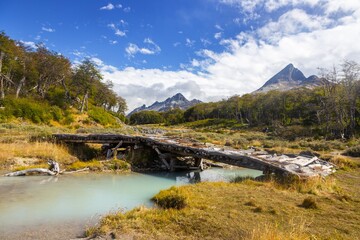 Old Decaying Wooden Pedestrian Bridge Across Glacial Meltwater Creek on Famous Laguna Esmeralda Hiking Trail.  Patagonia Mountain Range Landscape near Ushuaia Argentina on Clear Sunny Day