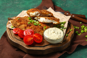 Board of tasty fried codfish with sauce on green background