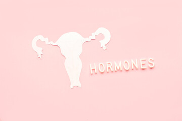 Word HORMONES with paper uterus on pink background