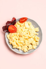 Plate of delicious scrambled eggs with tomatoes and basil on pale pink background
