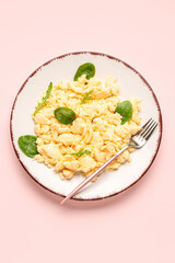 Plate of delicious scrambled eggs with herbs on pink background