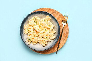 Plate of scrambled eggs with herbs on light blue background