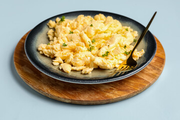 Plate of scrambled eggs with herbs on light blue background