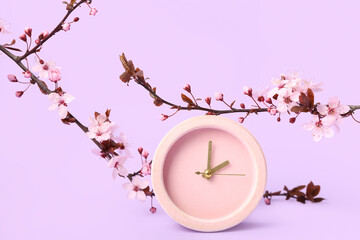 Blooming spring branches and clock on lilac background
