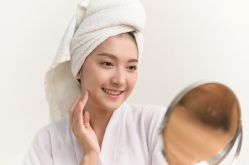 Close up portrait photo of young beautiful Asian woman taking care of her facial skin after apply face skin care cosmetic lotion moisturizer product and checking in mirror at home. Beauty care concept