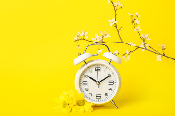 Blooming spring branches with chrysanthemums and white alarm clock on yellow background