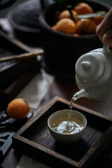 Porcelain and loquat fruit for making tea on wooden table, in oriental architectural interior, dark environment, close-up