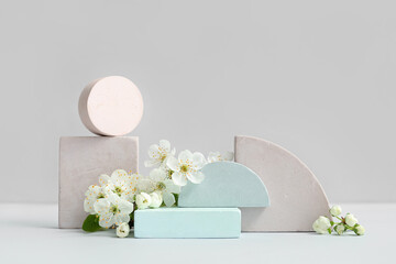 Decorative podiums and blooming branch on grey background