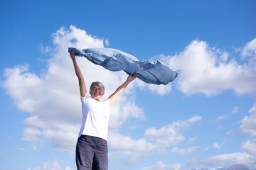 Cheerful senior woman standing outdoors with outstretched arms waving scarf in the blue sky enjoying freedom and vacation