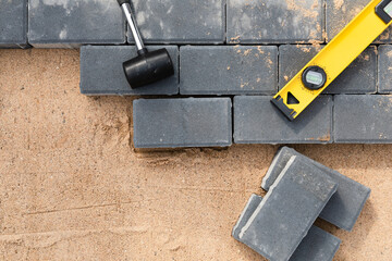 Laying cement pavement on a walkway with a rubber hammer and gloves on a sand. House improvement.