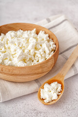 Bowl and spoon with tasty cottage cheese on light grunge background