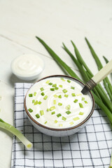 Bowl of tasty sour cream with green onion on light wooden background