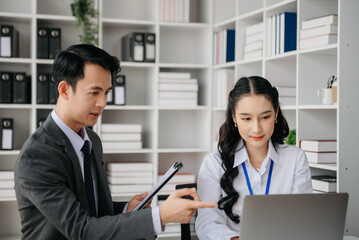 Fototapeta premium Asian business colleague business presents and explains and using laptop and tablet. Teamwork, financial marketing team, while sitting in office room.