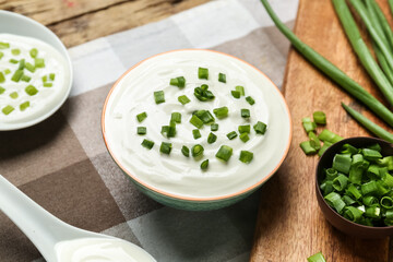 Bowl of tasty sour cream with green onion on table