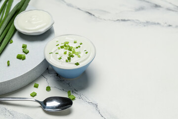 Bowls of tasty sour cream with green onion on white marble background