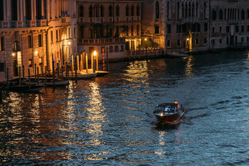 Lone motorboat floats the Grand Canal in Venice in glowing lights against the backdrop of blue...