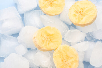 Sliced fresh banana and ice cubes on blue background