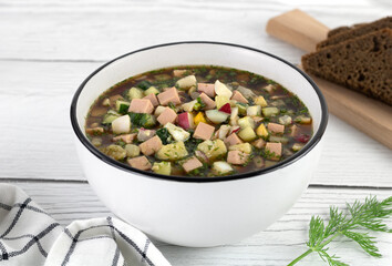 Okroshka - russian cold soup with vegetables, sausage, herbs, kvass and black bread on a black background.