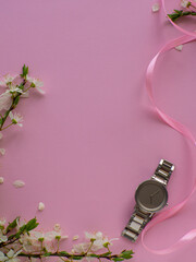 Womens wristwatch on pink background with cherry flowers and copy space