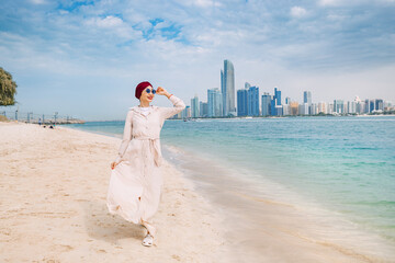 Young woman walks along sandy beach and takes occasional glances toward the impressive skyline,...