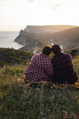 Travelers watch the sunset in the mountains.The couple meets the sunset in the mountains. Two travelers are sitting on the edge of a cliff and admiring the beautiful sunset. Panoramic view.