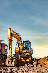 A wheeled excavator loads a dump truck with soil and sand. An excavator with a high-raised bucket...