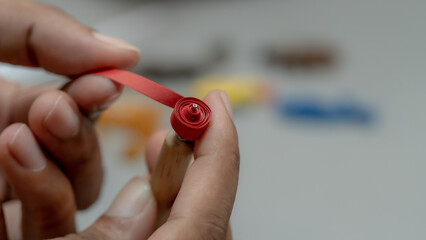 Crafting Creativity: Close-Up of Hand Rolling Red Paper Strips with Needle
