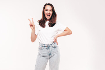 Obraz premium Young beautiful woman. Trendy carefree model in casual summer white T-shirt and blue jeans. Positive female isolated on white in studio. Cheerful and happy. Copy space, mockup. Shows peace sign