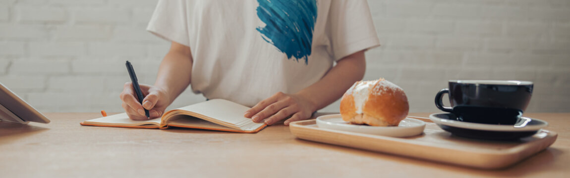 Young woman writing in notebook in coffee shop - Powered by Adobe