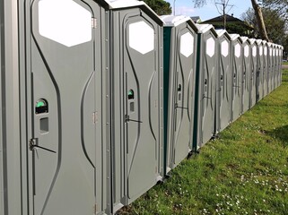 Row of brand new portable public toilets with the doors closed on a meadow.