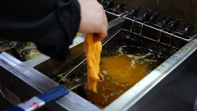 Cook putting meat in deep fryer in commercial kitchen, close up
