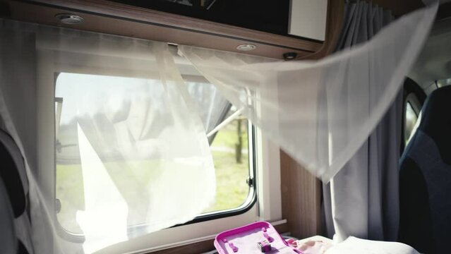 Wind plays with the curtains at the open window of a camper parked in the countryside