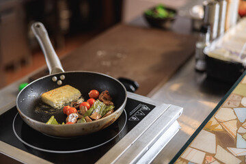 Tasty fried cheese with stewed vegetables is cooking on frying pan in restaurant kitchen
