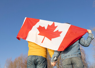 unrecognizable man and woman, holding hands, stand with a large Canadian flag behind their back...