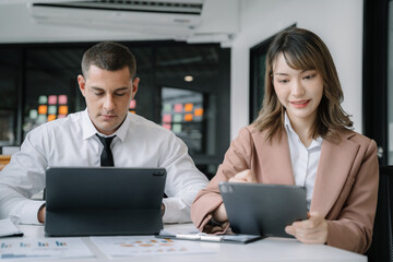 Business documents on office table with tablet and laptop computer and chart and two colleagues discussing data in office.