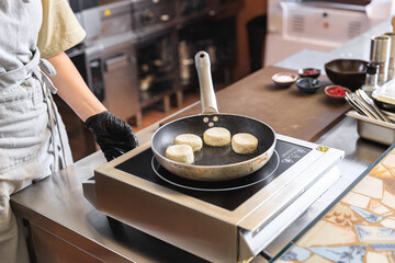 Professional Chef preparing cheesecakes on frying pan for breakfast in restaurant kitchen