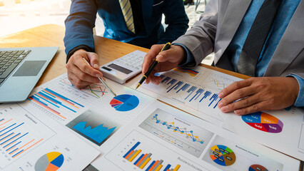 Business partners use laptops to analyze company financial budget reports, graphs and progress of...